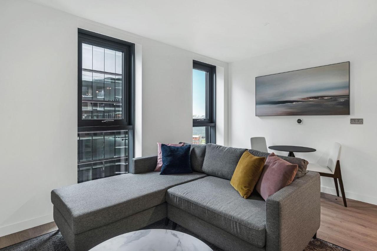 Citysuites 2 Aparthotel Σάλφορντ Εξωτερικό φωτογραφία The photo shows a modern living space featuring a gray sectional sofa adorned with colorful throw pillows. There are large windows allowing natural light to fill the room, offering a view of the outdoors. A wall-mounted television is positioned above