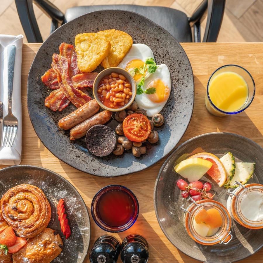Citysuites 2 Aparthotel Σάλφορντ Εξωτερικό φωτογραφία The photo showcases a delicious breakfast spread. On a large, dark plate, there are items including crispy bacon, two fried eggs, baked beans, a grilled tomato, sautéed mushrooms, sausage links, and slices of black pudding. There's also a few pieces 