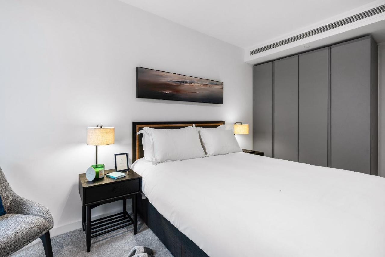 Citysuites 2 Aparthotel Μάντσεστερ Εξωτερικό φωτογραφία The photo shows a modern bedroom with a neatly made bed featuring white linens and pillows. Flanking the bed are two bedside tables, each with a lamp providing soft lighting. There is a piece of artwork above the bed, which appears to depict a landsc