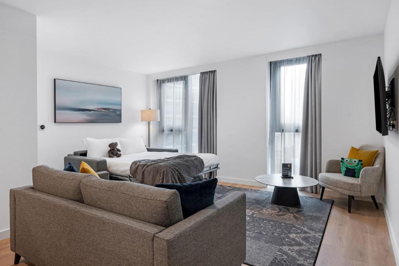 Citysuites 2 Aparthotel Μάντσεστερ Εξωτερικό φωτογραφία The photo shows a modern living space that incorporates a cozy and inviting atmosphere. It features a light-colored couch with colorful cushions, positioned in front of a coffee table. There's a comfortable armchair nearby, and a throw blanket is dra
