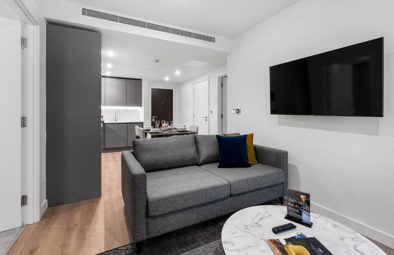 Citysuites 2 Aparthotel Μάντσεστερ Εξωτερικό φωτογραφία The photo shows a modern living space that includes a gray sofa with colorful cushions, a round marble coffee table, and a flat-screen TV mounted on the wall. In the background, there is a kitchen area featuring sleek cabinets. The flooring is light 