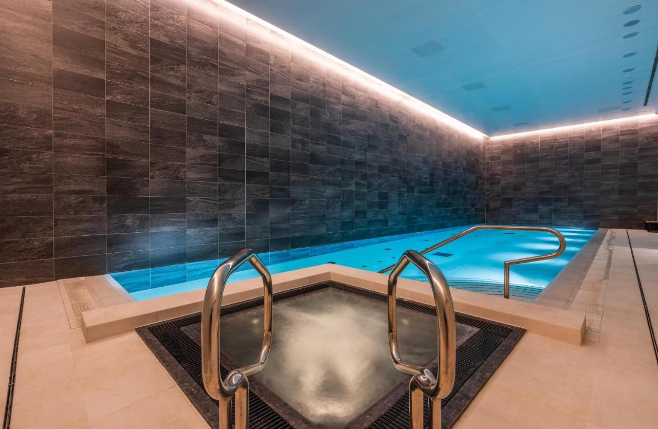 Citysuites 2 Aparthotel Μάντσεστερ Εξωτερικό φωτογραφία The photo shows a modern indoor swimming pool area. The pool features a sleek, rectangular design with a beautiful blue water that seems illuminated. Surrounding the pool are dark, textured walls, adding to the elegant atmosphere. There are dual meta