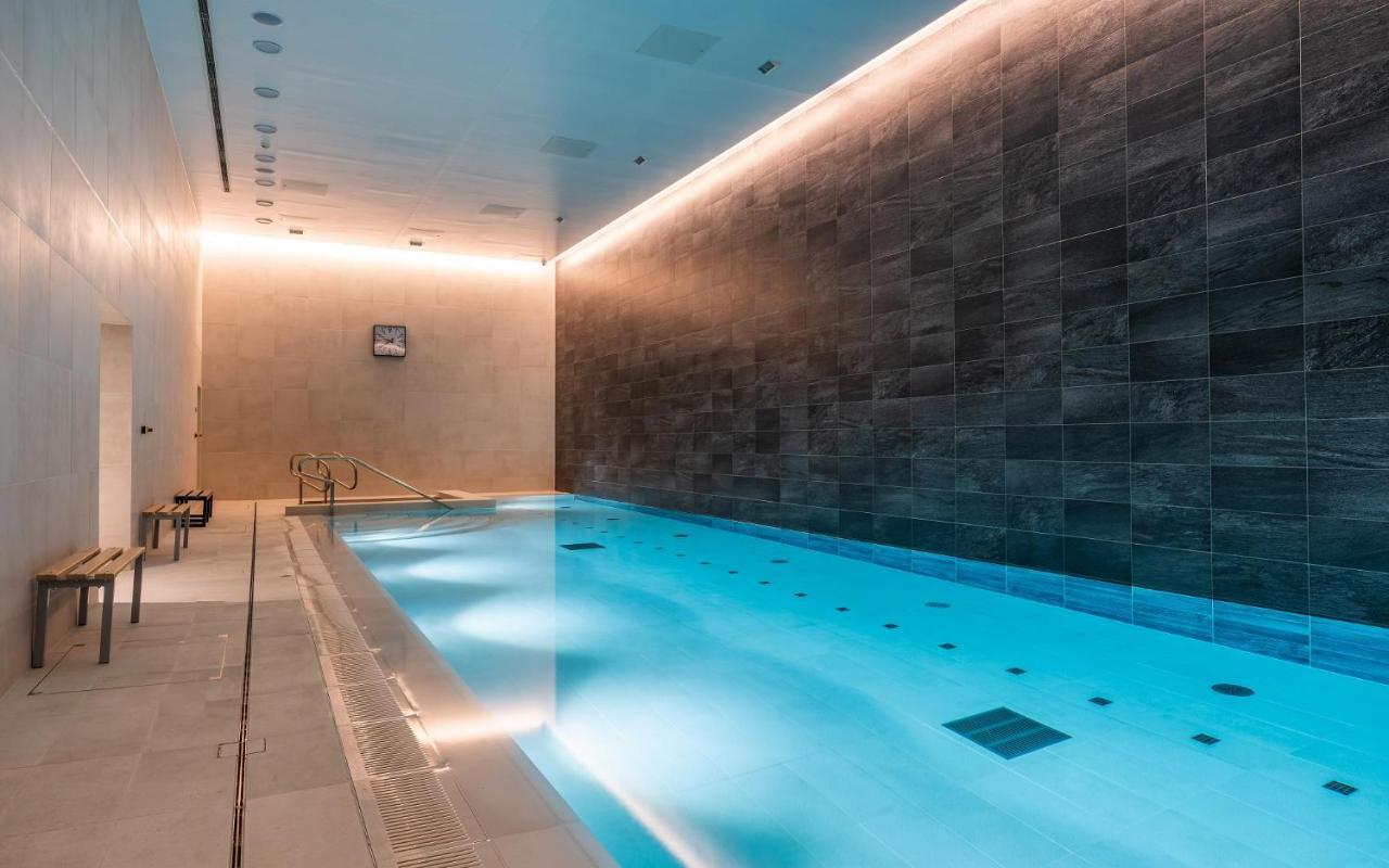 Citysuites 2 Aparthotel Μάντσεστερ Εξωτερικό φωτογραφία The photo shows an indoor swimming pool area. The pool is illuminated with a soft blue light, creating a calming atmosphere. The walls are designed with dark tiles, and there is a lighter tiled area surrounding the pool. Ambient lighting is installed