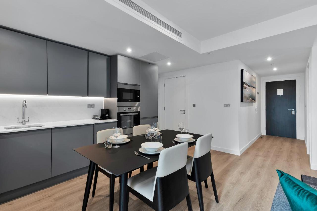 Citysuites 2 Aparthotel Μάντσεστερ Εξωτερικό φωτογραφία The image shows a modern kitchen and dining area. The kitchen features sleek gray cabinets with a white countertop, and it is equipped with appliances such as a microwave. There’s a dining table set for four, with white plates and glasses ready. The 