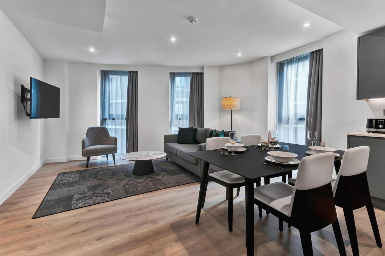 Citysuites 2 Aparthotel Μάντσεστερ Εξωτερικό φωτογραφία The photo shows a modern living space that includes a living area and dining area. 

- **Living Area**: There's a gray sofa with a coffee table in front of it, along with a single armchair. A large flat-screen TV is mounted on the wall. The space is 