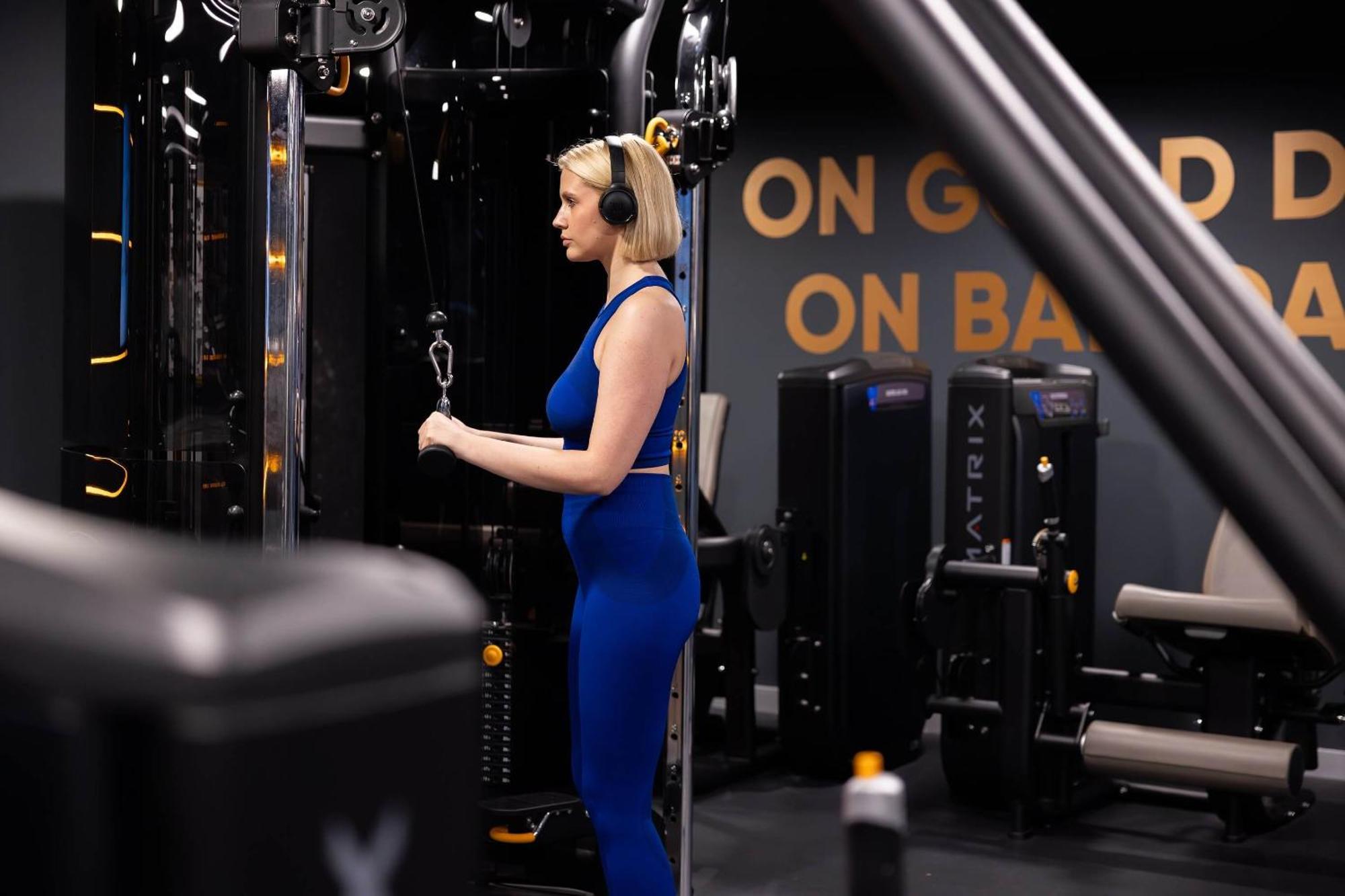 Citysuites 2 Aparthotel Μάντσεστερ Εξωτερικό φωτογραφία The photo shows a woman working out in a gym. She is wearing a blue athletic outfit and headphones while using a gym machine. The background features various other gym equipment and a wall with the words "ON GOOD ON BAD" displayed prominently. The se