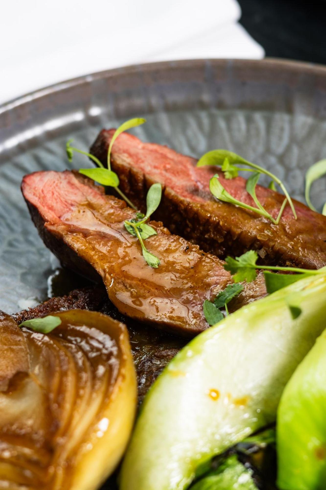 Citysuites 2 Aparthotel Σάλφορντ Εξωτερικό φωτογραφία The photo features slices of meat, likely beef, presented on a decorative plate. The meat appears to have a rich brown sauce drizzled over it and is garnished with fresh herbs, adding a pop of green. There are also some slices of a light-colored vege