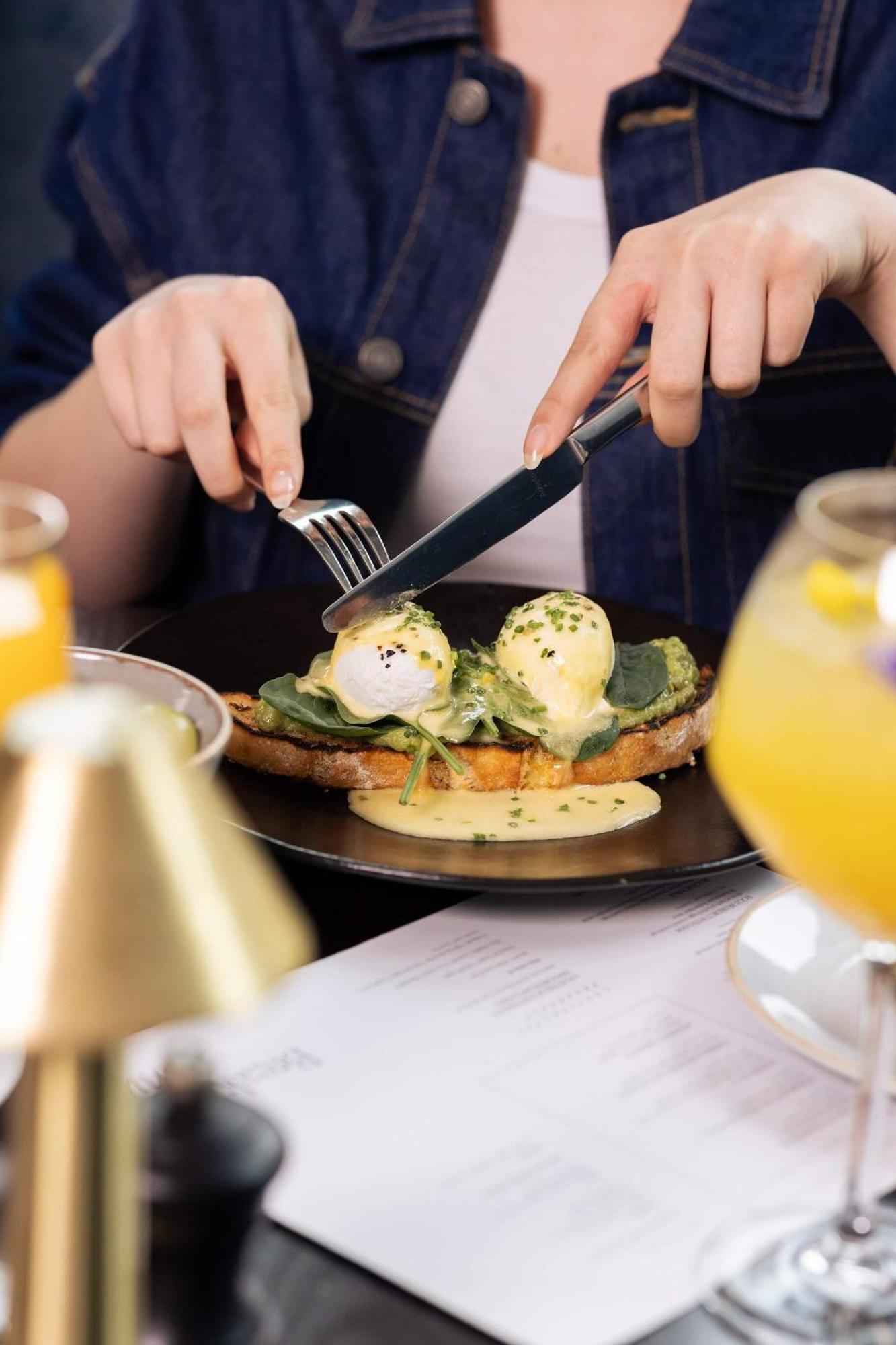Citysuites 2 Aparthotel Σάλφορντ Εξωτερικό φωτογραφία The photo shows a person preparing to eat a dish of eggs Benedict. They are holding a knife and fork, ready to cut into the meal, which features poached eggs on top of a slice of toast, accompanied by spinach and a creamy hollandaise sauce drizzled o